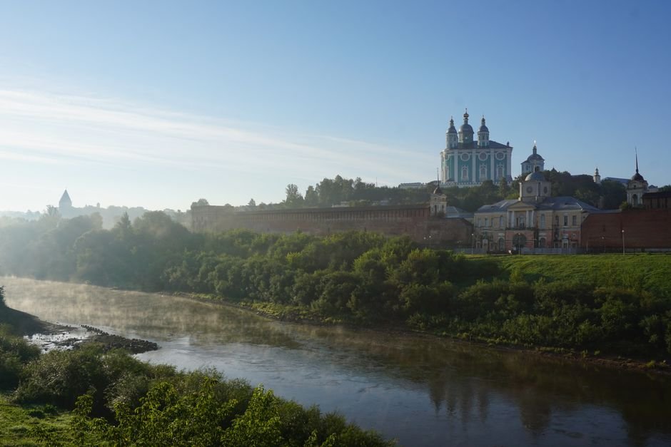 View of the Smolensk Kremlin and Assumption Cathedral by the river at sunrise, showcasing historic architecture.