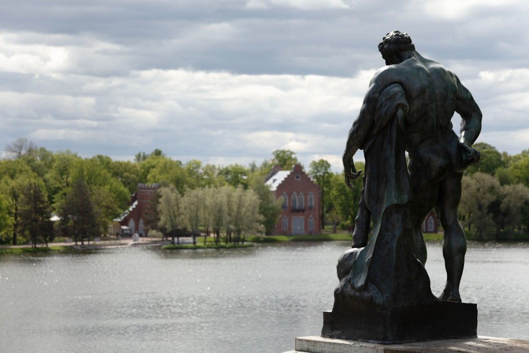 A statue stands near a lake and lush scenery